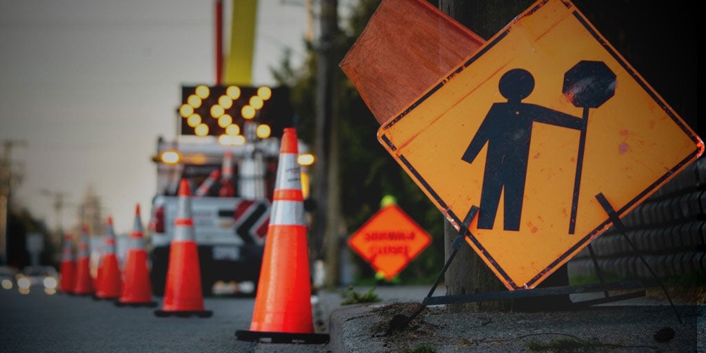 Street under construction containing traffic cones and caution sign.